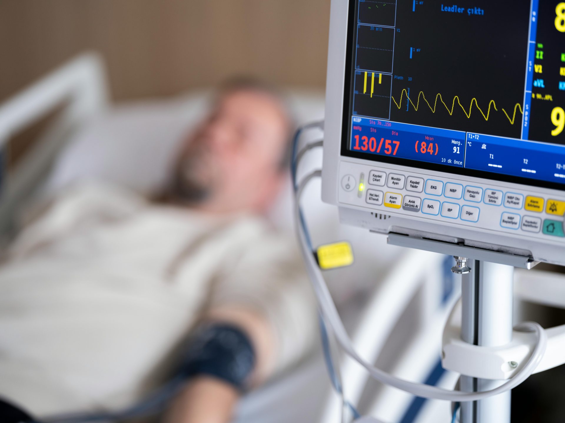 Patient im Krankenhausbett mit Herzmonitor, der Blutdruck und Herzfrequenz anzeigt.